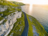 A winding coastal road with waves crashing against the cliffs under a golden sunset.