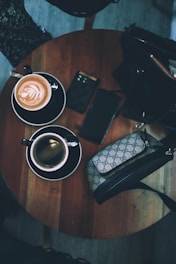 A stylish canvas tote bag with leather handles resting on a wooden table beside a coffee cup.