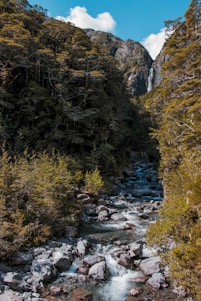 A serene mountain stream flowing through rocky terrain under clear blue skies, capturing the essence of Himalayan purity.