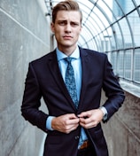 man wearing black and teal dress suit standing near gray wall