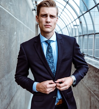 man wearing black and teal dress suit standing near gray wall