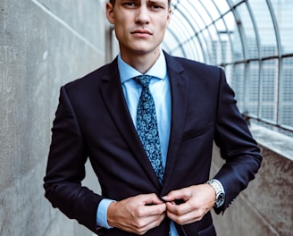 man wearing black and teal dress suit standing near gray wall