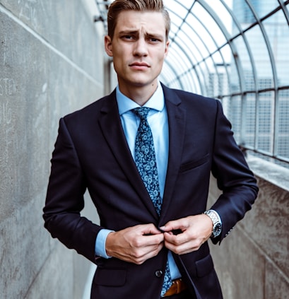 man wearing black and teal dress suit standing near gray wall