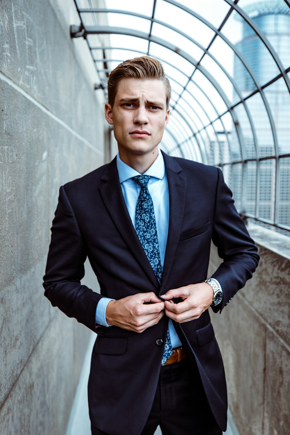 man wearing black and teal dress suit standing near gray wall