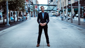 A person in a suit stands confidently in the middle of a city street, surrounded by urban buildings, trees, and street furniture. The environment features a blend of modern architecture and city elements.