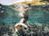 Underwater shot of a snorkeler reaching out to colorful fish around a coral reef.