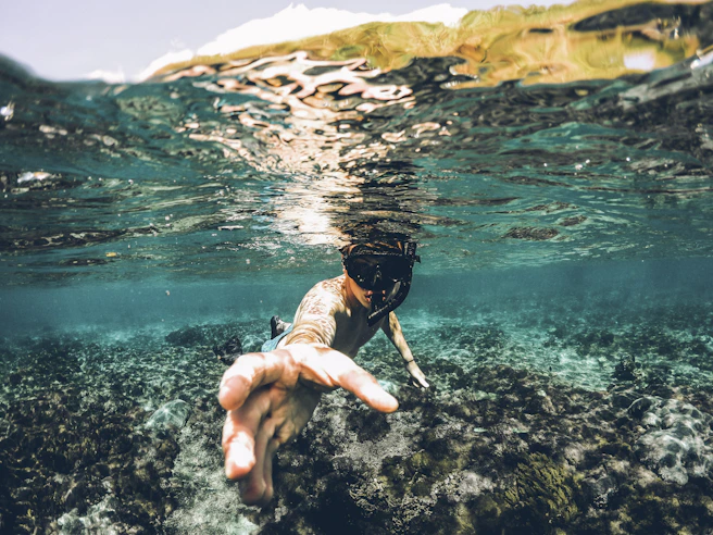 underwater photography of man wearing snorkel lending his hand