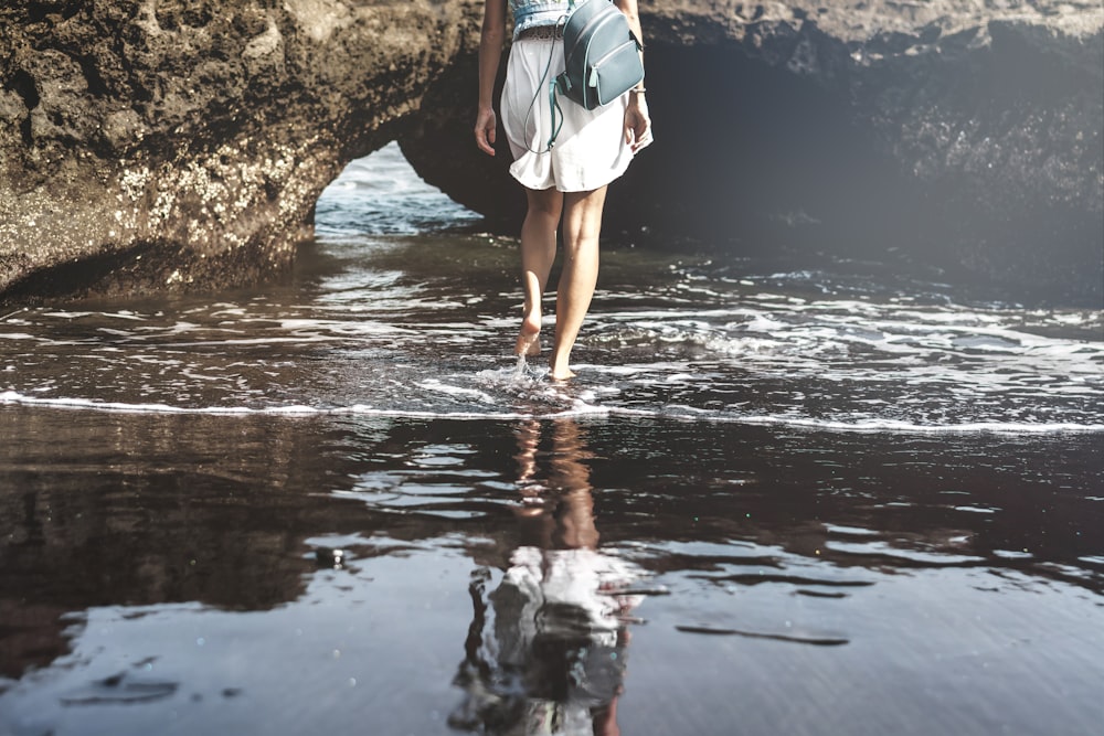 person carrying black backpack stepping on body of water