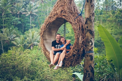 man and woman riding on brown hammock beside brown tree