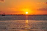 A vibrant sunset casting golden hues over the sails as the boat cuts through calm seas.