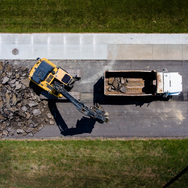 aerial photography of yellow heavy equipment beside white dump truck at daytime