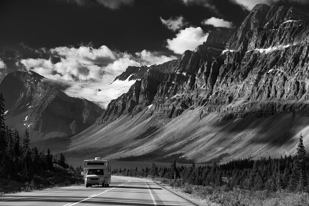 grayscale photo of vehicle passing on road near mountain range