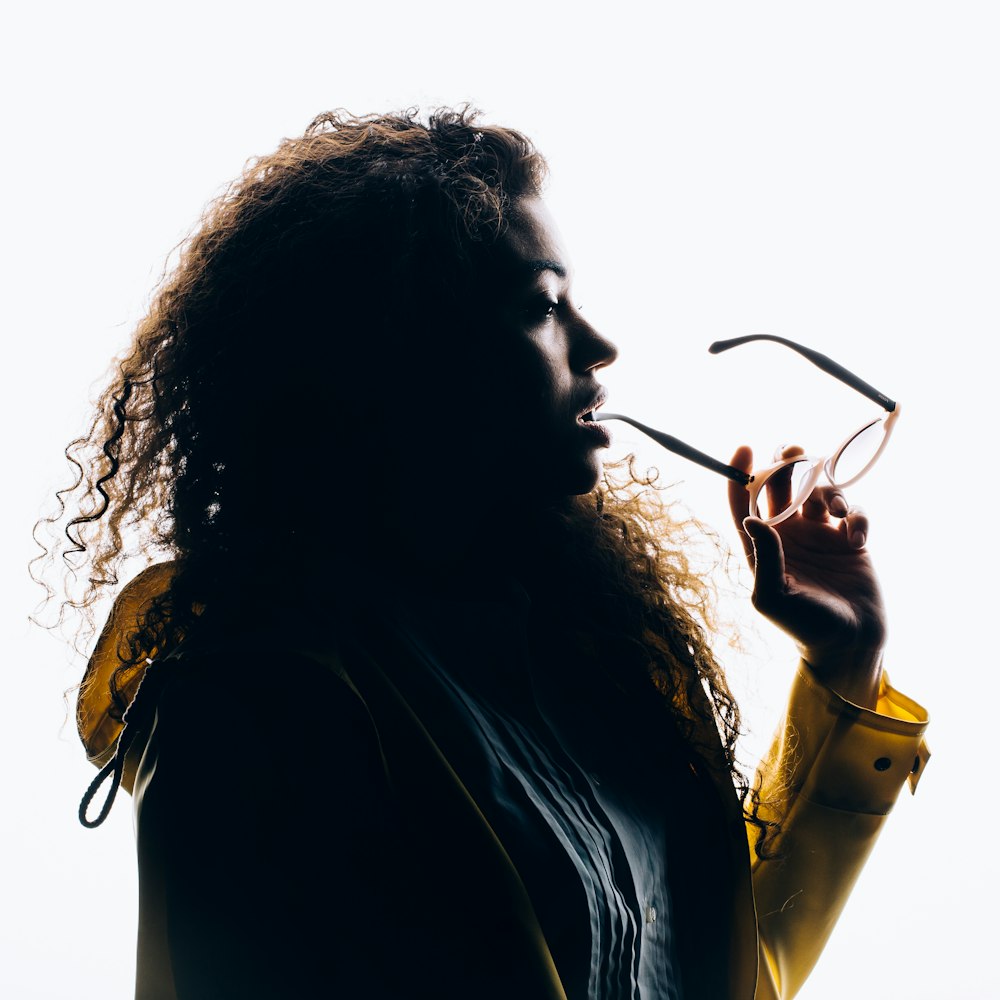 silhouette photo of woman biting her eyeglasses