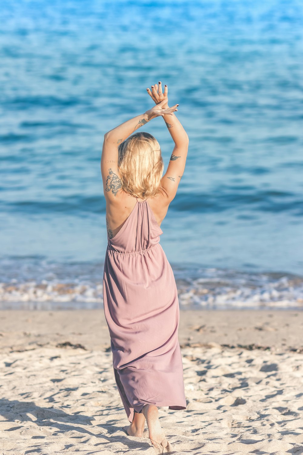 mulher usando vestido rosa levantando as duas mãos enquanto caminha na costa