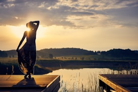 silhouette of woman standing on brown wooden dock during golden hour