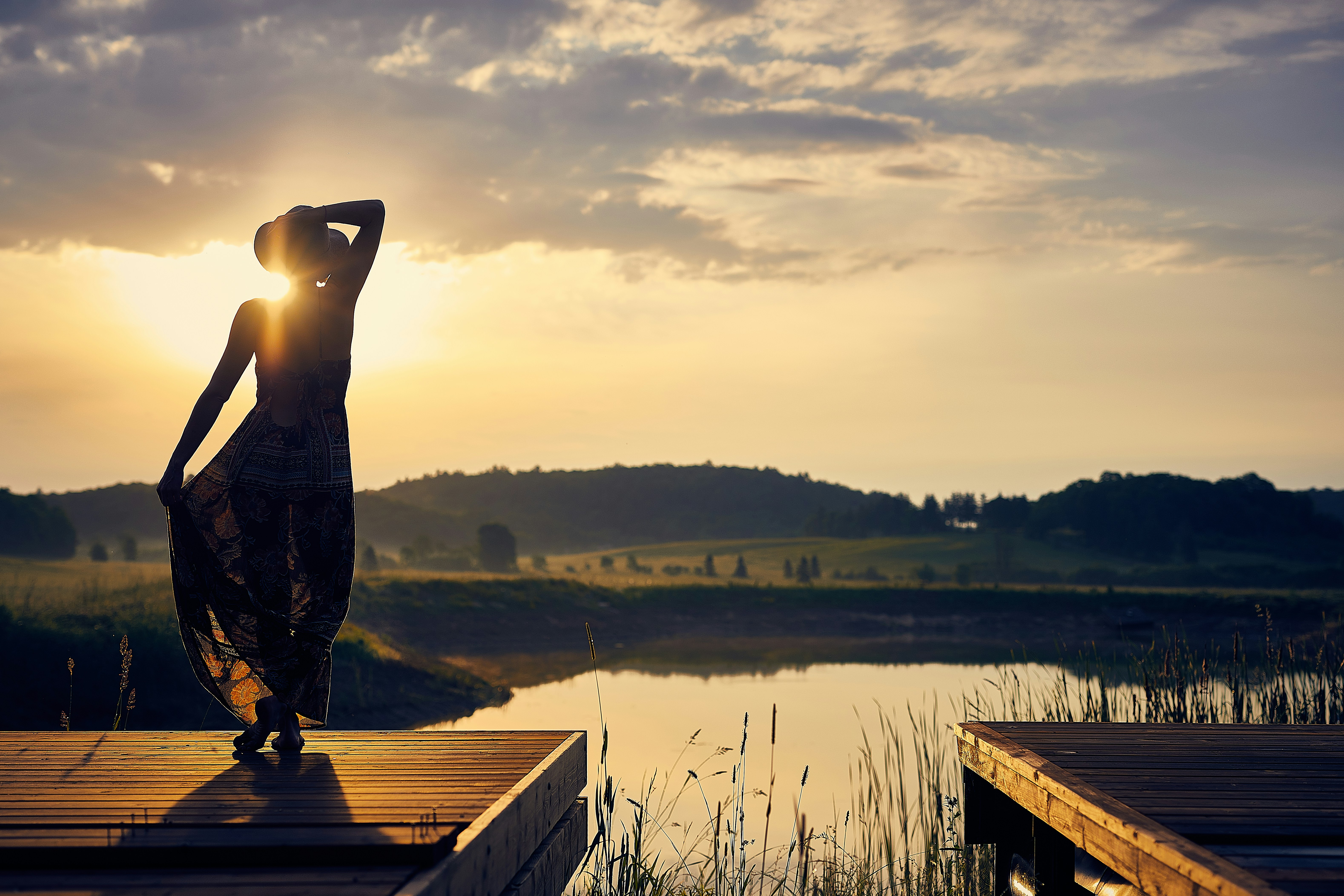 silhouette of woman standing on brown wooden dock during golden hour