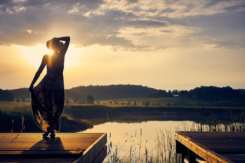 silhouette of woman standing on brown wooden dock during golden hour