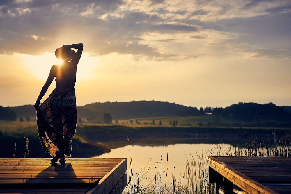 silhouette di donna in piedi sul molo di legno marrone durante l'ora d'oro