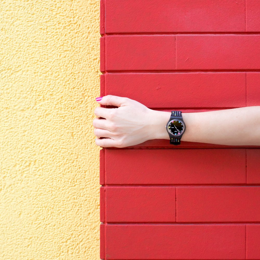 빨간 벽돌 벽을 들고 검은 아날로그 시계를 착용 한 사람