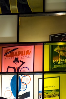 A series of posters for films are displayed behind glass panels, each tinted with different colors like pink, yellow, and dark green. One poster prominently features a stylized illustration of Charlie Chaplin.