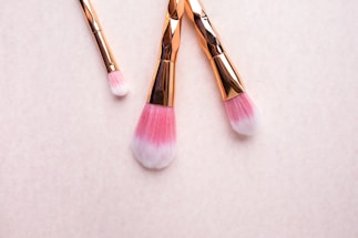 Softly lit close-up of a rose gold makeup brush resting on a blush pink surface.