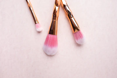 Golden makeup brushes arranged neatly on a soft nude-colored fabric, catching natural light.