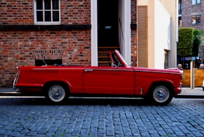 A gleaming vintage red convertible parked on a sunlit cobblestone street.