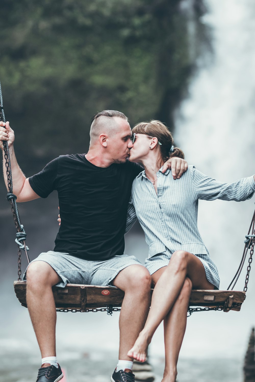 man and woman kissing while riding on swing bench