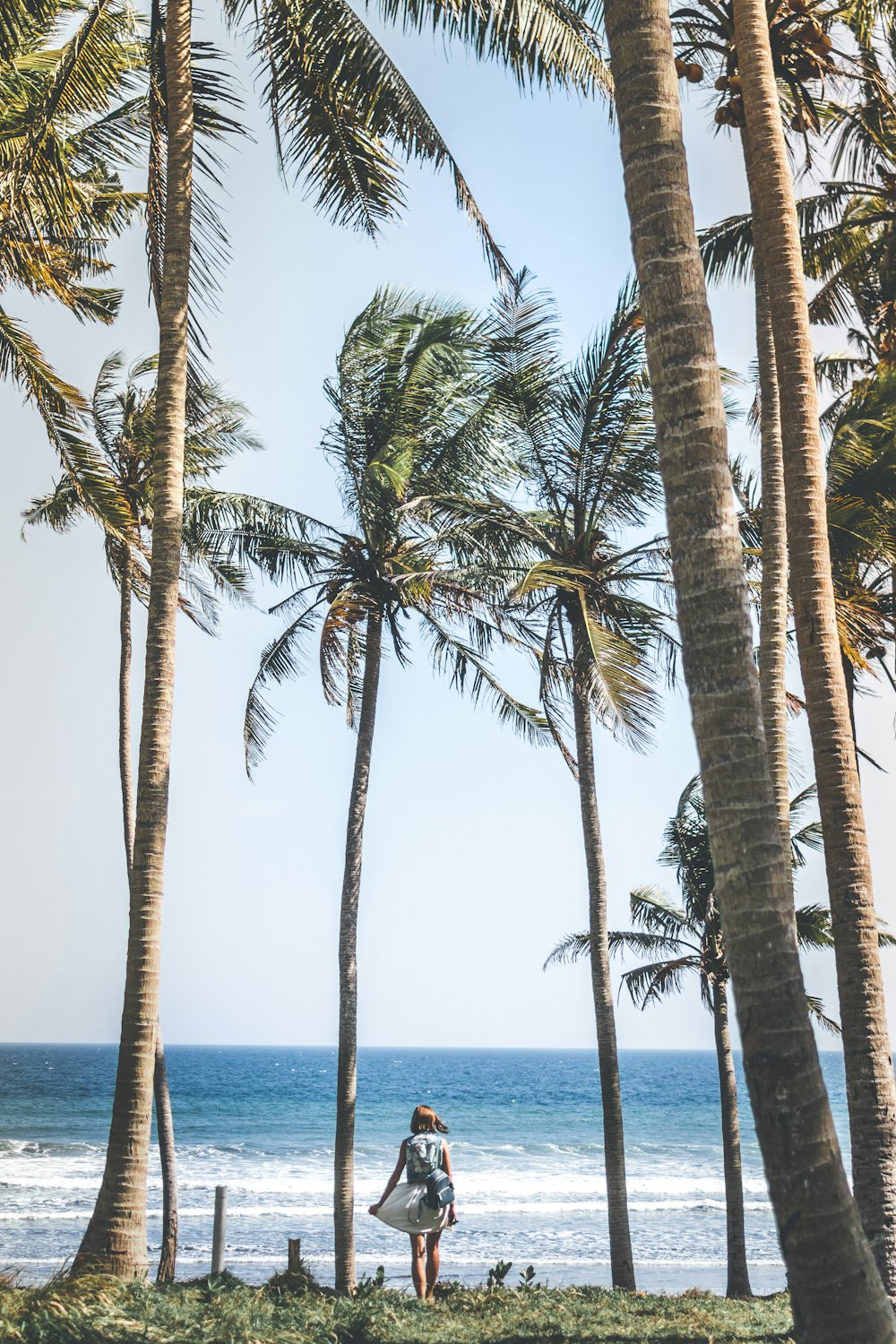 woman in gray dress near seashore under coconut trees