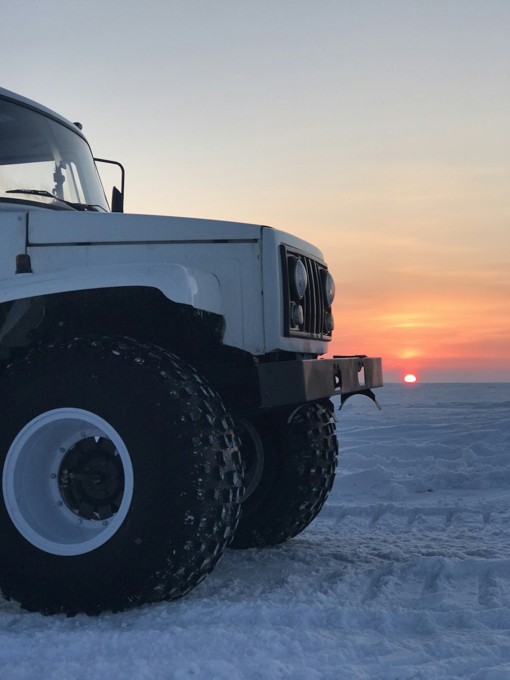 white vehicle parked on seashore with background of sunset