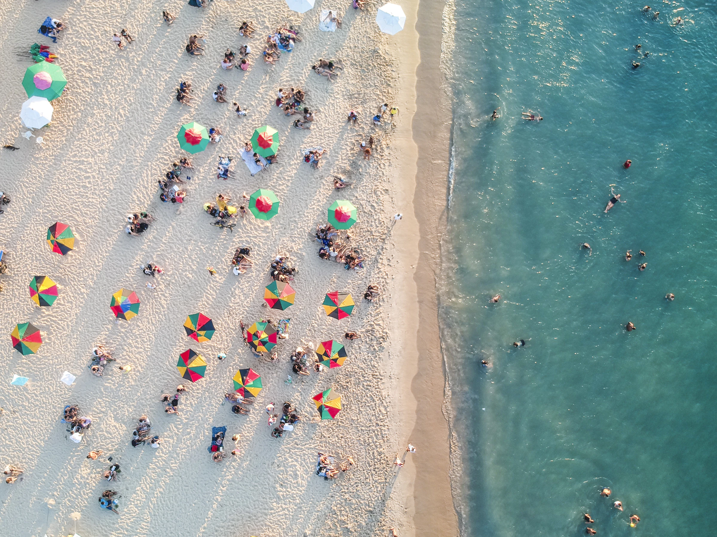 Beach umbrellas and shades seen from above along the shoreline
