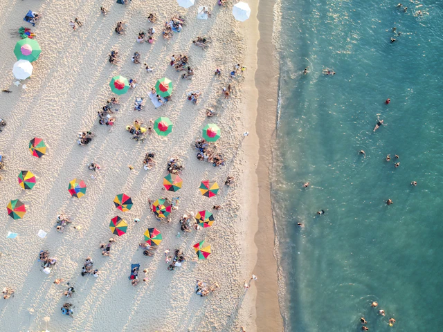 Beach umbrellas and shades seen from above along the shoreline