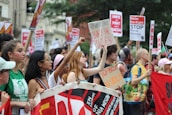 A large group of people participating in a protest, holding signs that display messages against racism and fascism. The crowd is diverse, consisting of men and women of various backgrounds. Many are holding banners and placards with bold text advocating for solidarity and equality.