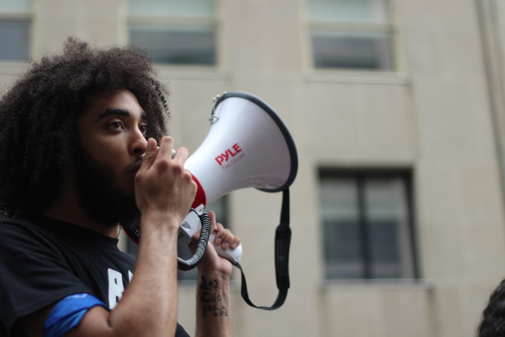 selective focus photography of man holding loudspeaker beside building