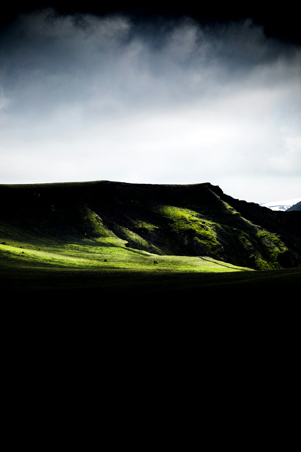 a grassy hill with a dark sky in the background