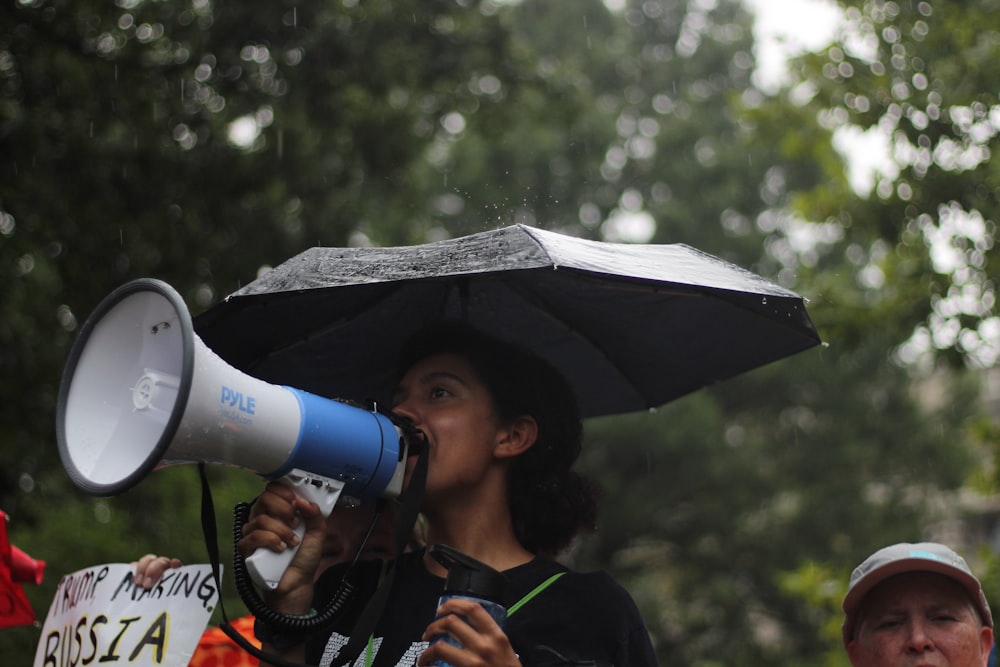 mulher em pé segurando guarda-chuva e megafone branco durante o dia