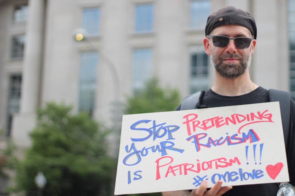 man holding stop pretending your racism is patriotism!!! signage