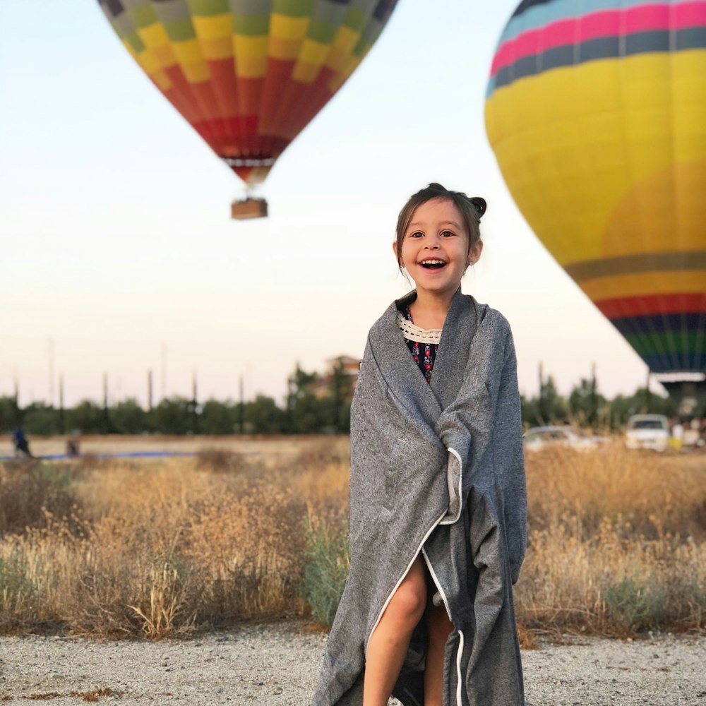 selective focus photography of girl covered by gray scarf with background of hot air balloons