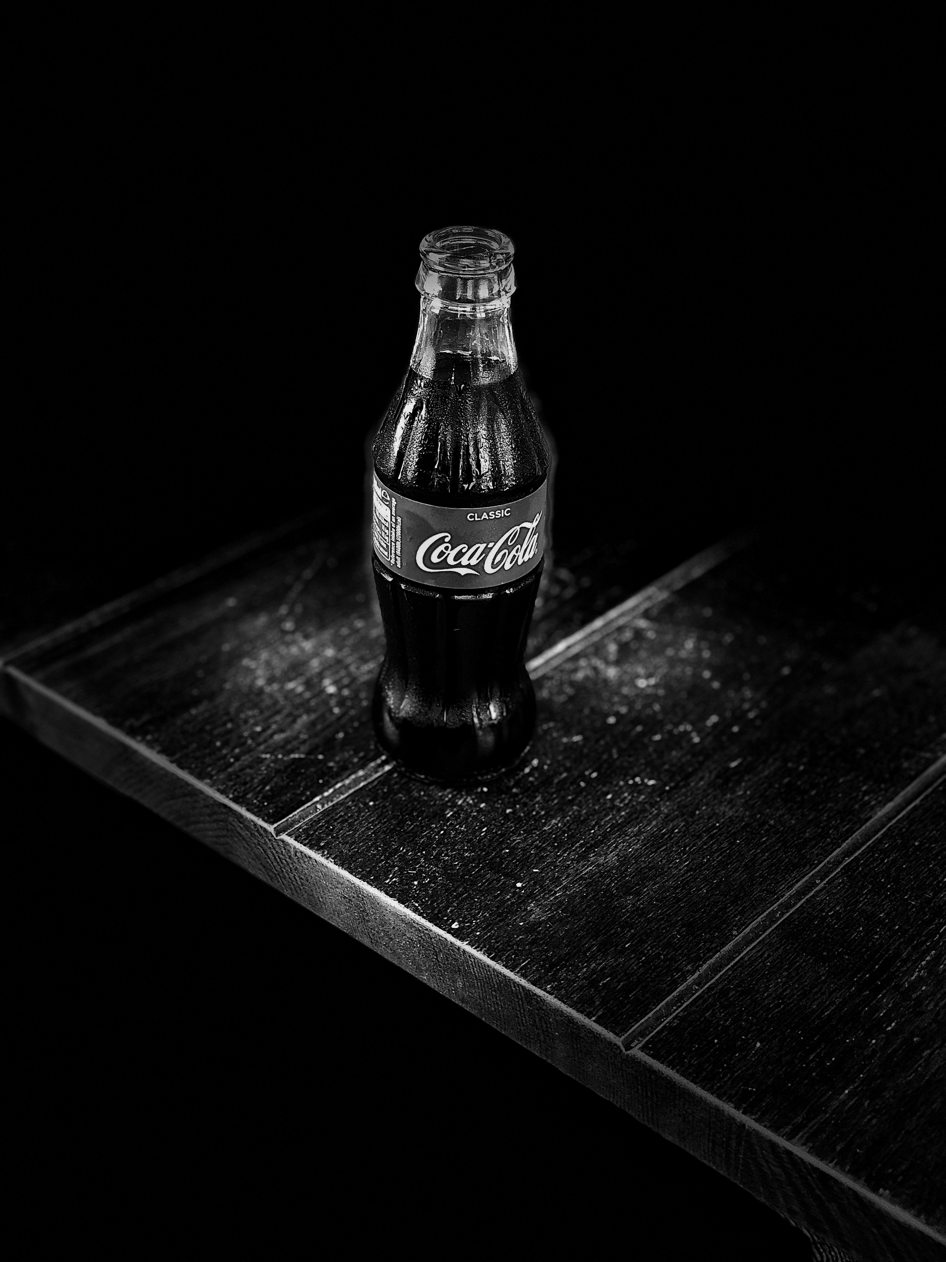grayscale photography of Coca-Cola bottle on table