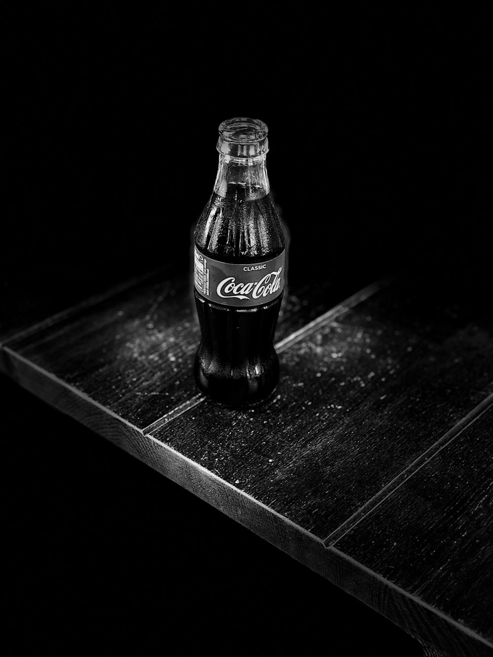 grayscale photography of Coca-Cola bottle on table