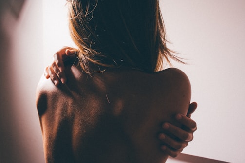 A softly lit scene showing a woman’s silhouette embracing herself, symbolizing sensuality and connection.