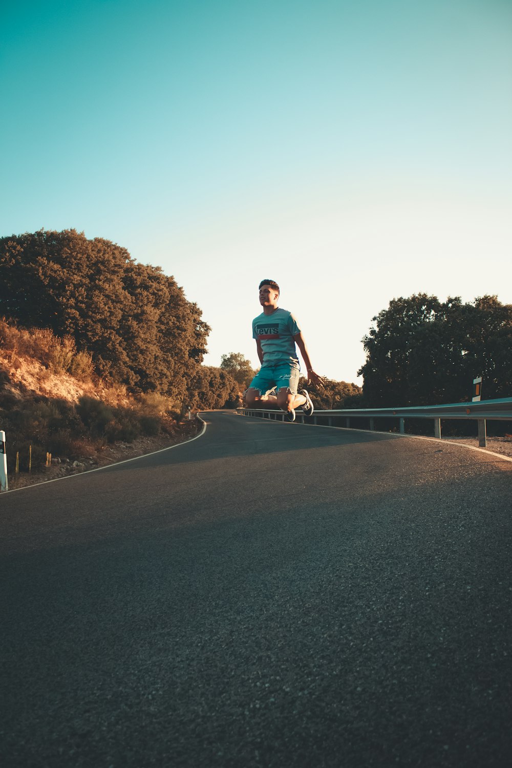 man jumping on concrete road near brown trees at daytime