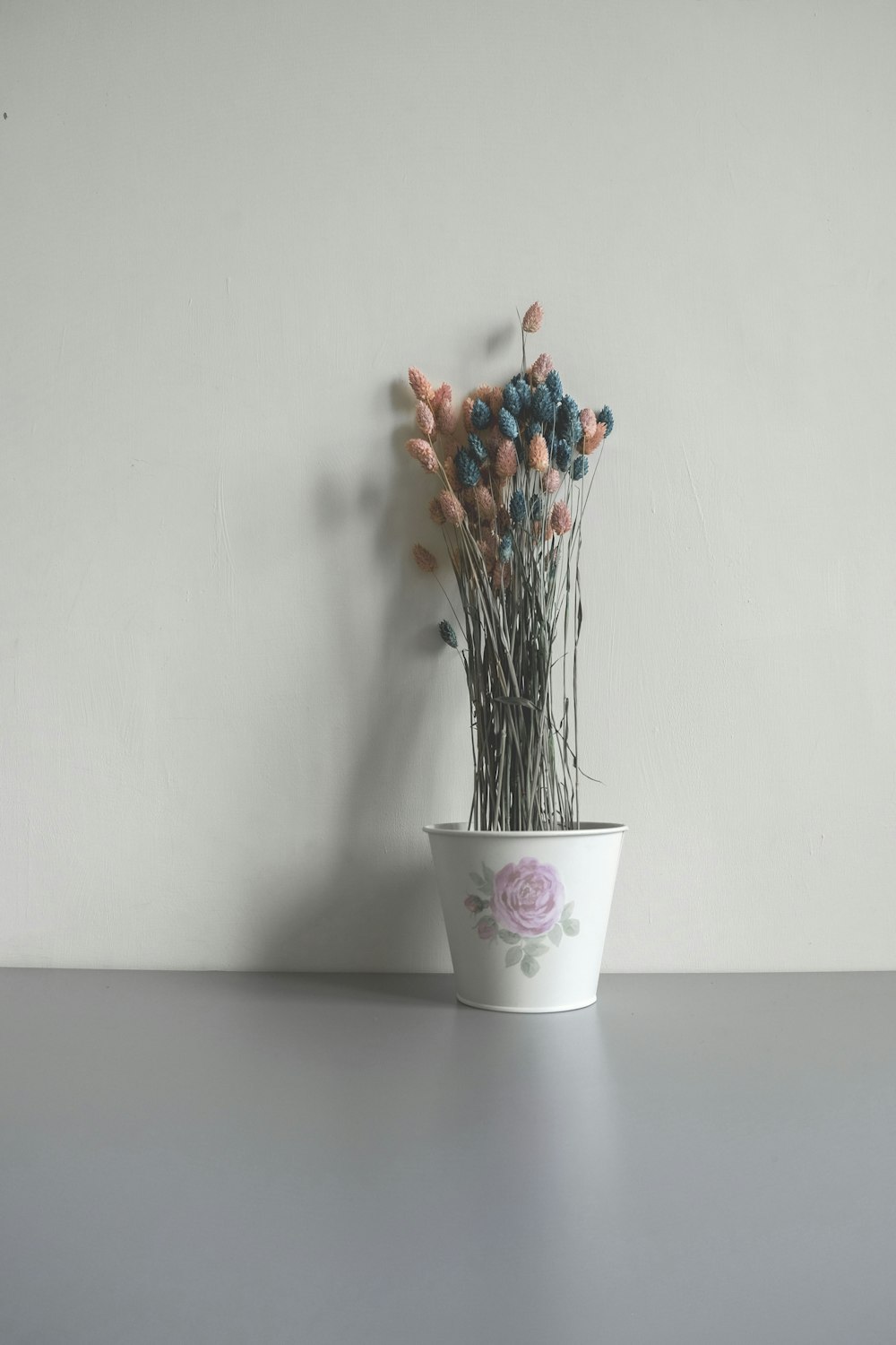 white potted pink and blue artificial flowers near wall
