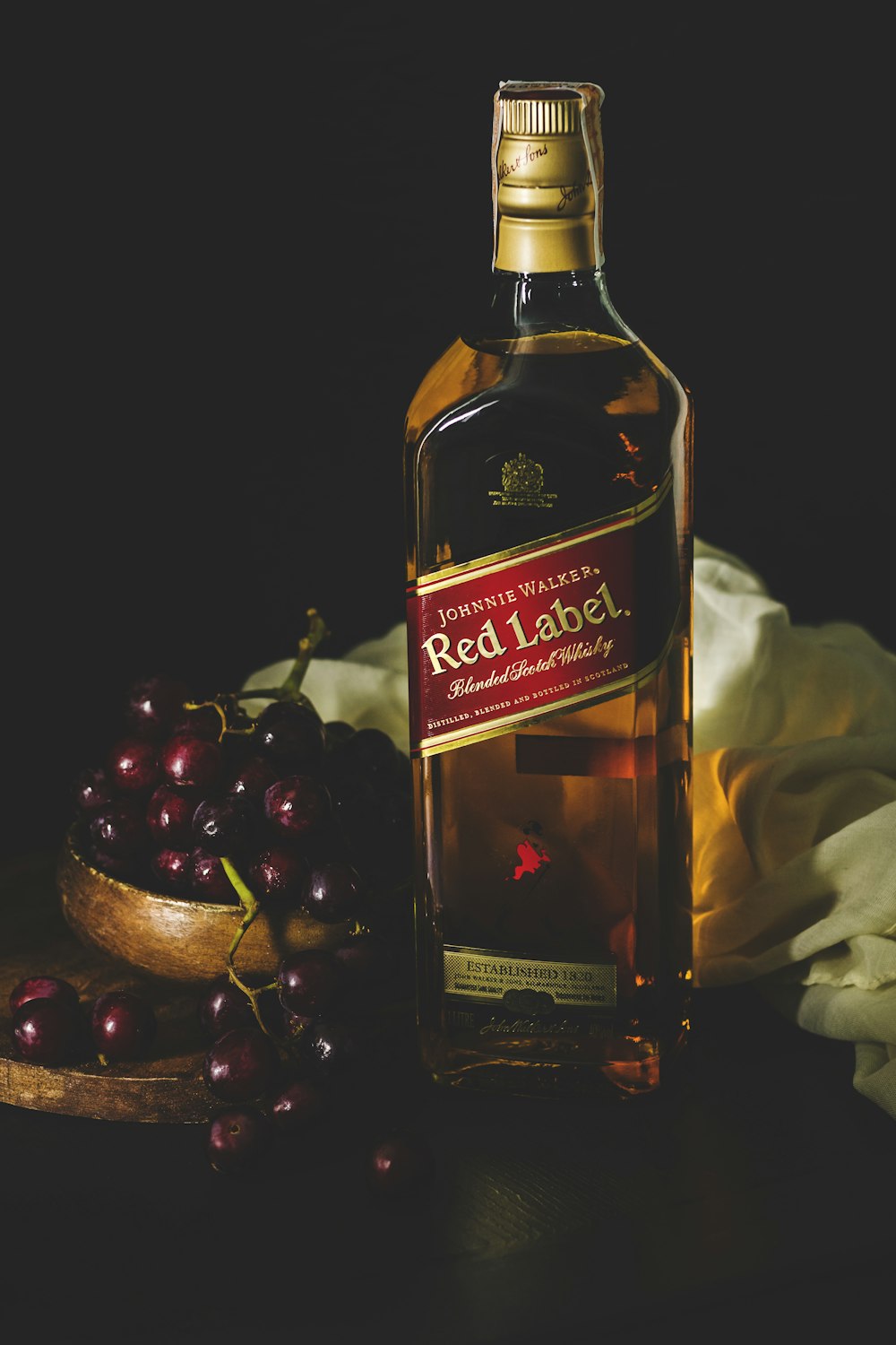 Johnnie Walker red label bottle beside bowl of red grapes