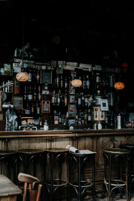 Warmly lit bar counter with a row of colorful cocktails and rustic wooden stools.