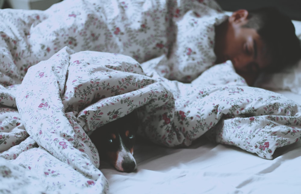 homem deitado na cama ao lado de cachorro preto de pelo curto