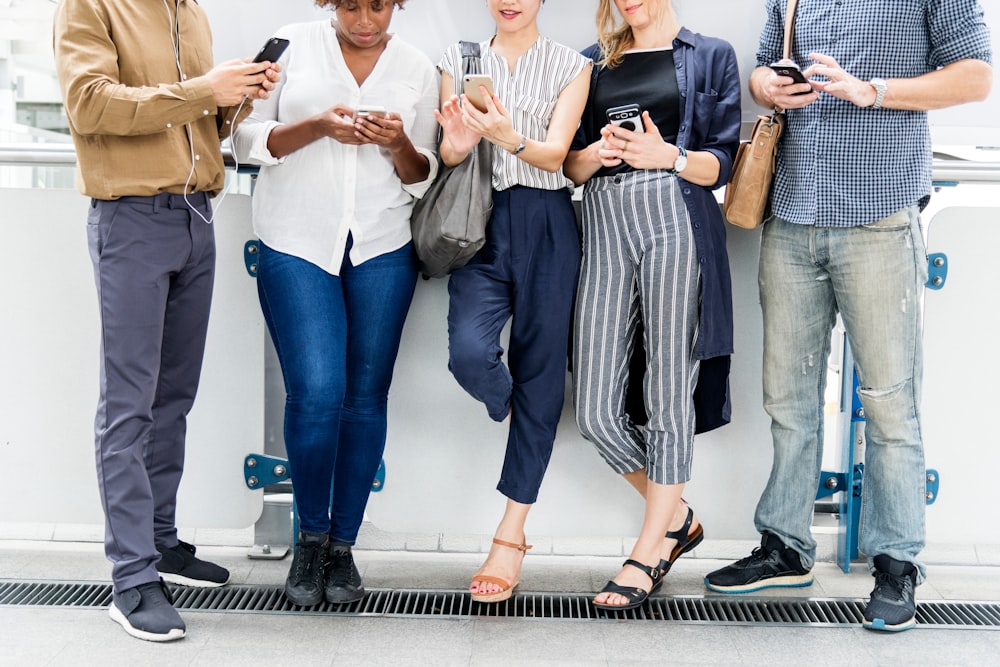 five person standing while using smartphone