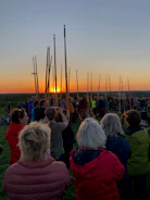 A group of people gathered outdoors praying together at sunset.
