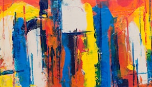 An abstract painting with bold and energetic brushstrokes, featuring a mix of vibrant colors including blue, orange, yellow, and white. The arrangement is chaotic yet harmonious, with drips and smudges that create a sense of movement and depth.