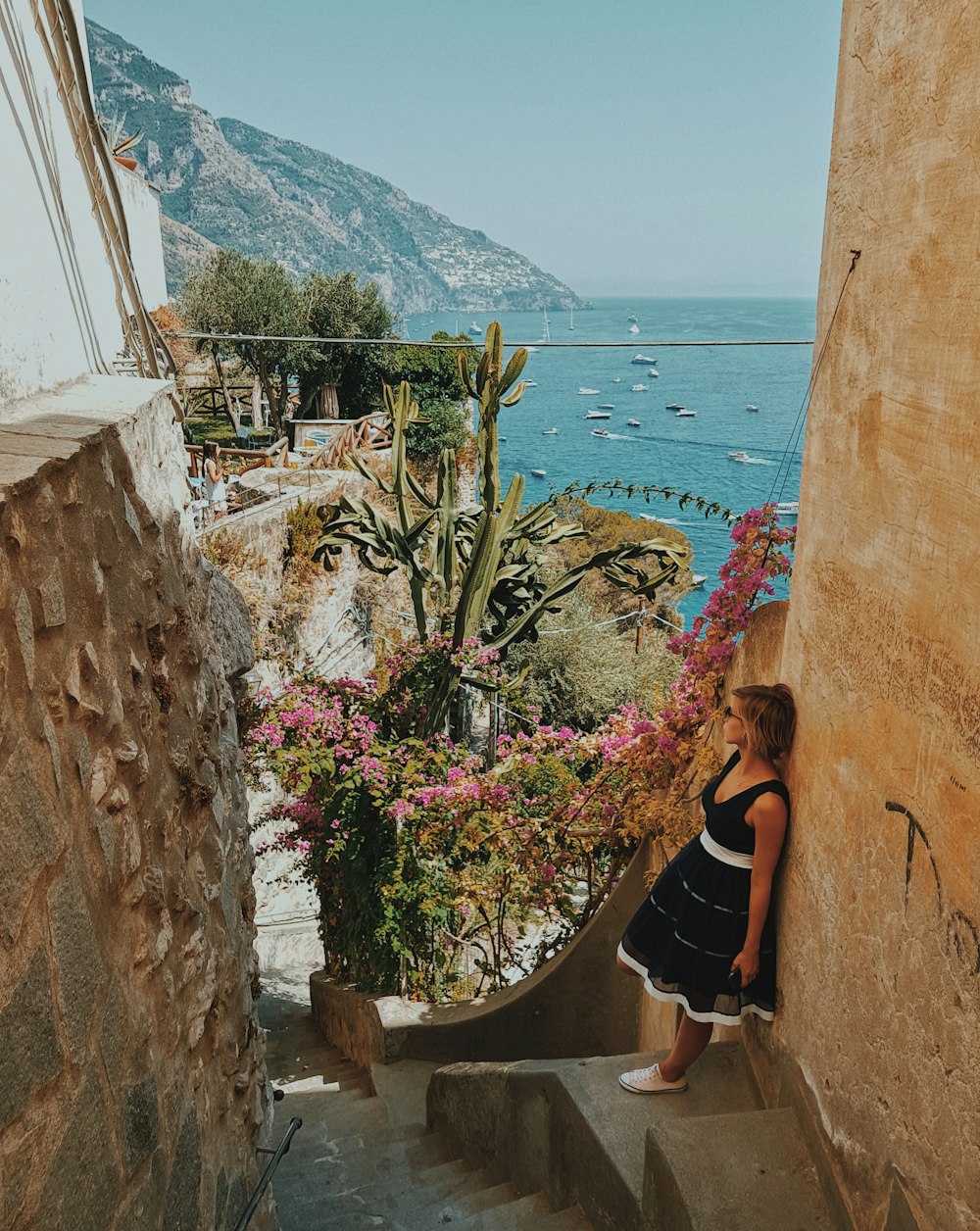 Donna che si appoggia al muro di cemento marrone vicino ai fiori dai petali rosa